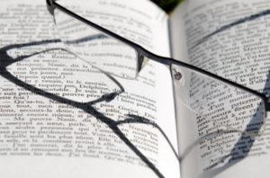 Foto mostra livro aberto em ‘close’ com visível divisão em parágrafos e um par de óculos de leitura repousando sobre suas páginas