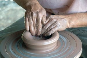 Duas mãos moldando cerâmica.